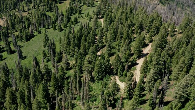 Aerial following winding alpine road across ridge in green mountains