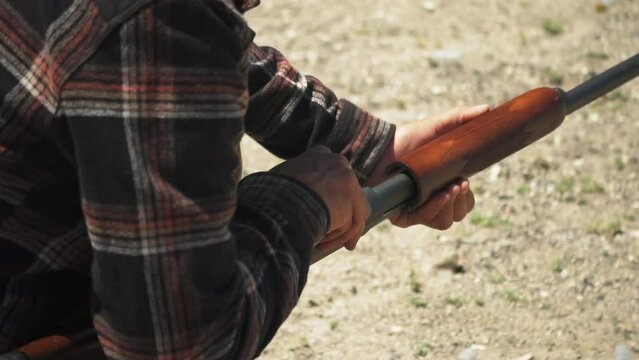 Man wearing a checkered shirt reloads slugs into pump action shotgun, slow motion