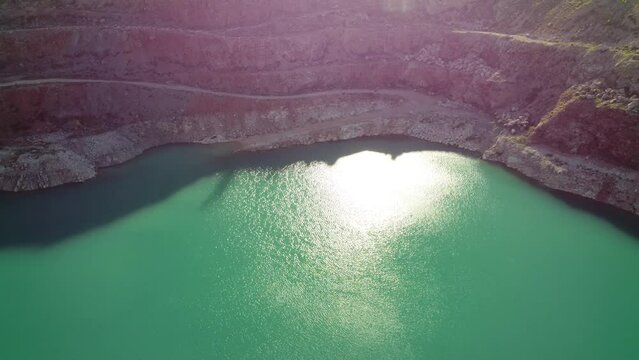 Aerial top view on opencast mining quarry with flooded bottom, turquoise surface of the lake. Quarry pond overgrown with green plants and clear turquoise water