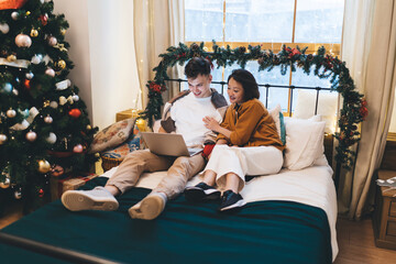 Couple watch on laptop on bed near christmas tree