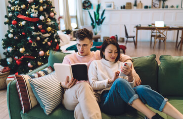 Man read book and girl use smartphone on sofa