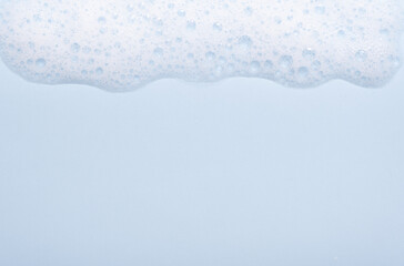 Face cleansing mousse sample. White cleanser foam bubbles on blue background. Soap, shower gel, shampoo foam texture closeup