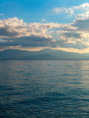 Cloudy sky above the sea and mountains in the horizon's background. The change of weather is continuous in all seasons. Calm and serene, scenic view.