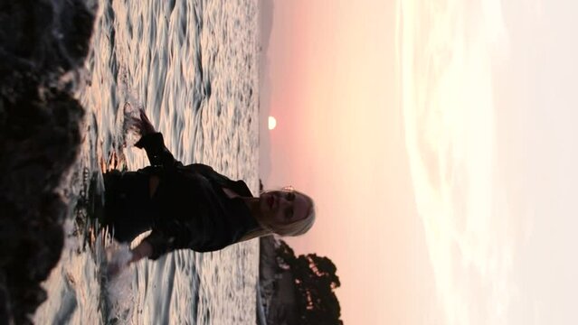 Attractive blonde girl in the Adriatic Sea, wearing a black shirt with glasses, splashes and poses in the water during the sunset in Dubrovnik, Croatia.