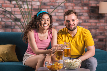 In front of tv good looking couple very excited watching a football match they are getting happy when favourite team wins they cheers with beer and enjoy the evening