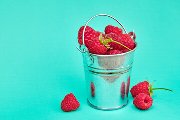 Fresh ripe raspberries in a metal small bucket on light emerald background.