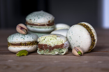 Homemade pistachio and chocolate macaroons stacked up on wooden table with pistachio nuts