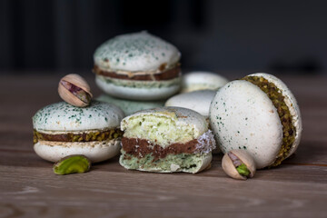 Homemade pistachio and chocolate macaroons stacked up on wooden table with pistachio nuts