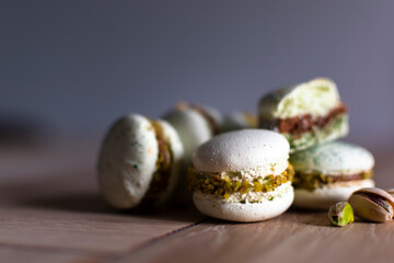 Homemade pistachio and chocolate macaroons stacked up on wooden table with pistachio nuts