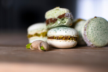 Homemade pistachio and chocolate macaroons stacked up on wooden table with pistachio nuts