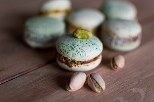 Homemade pistachio and chocolate macaroons stacked up on wooden table with pistachio nuts