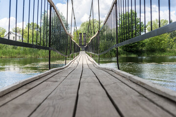 Fototapeta premium Wooden suspension bridge across the lake. Pedestrian walkway made of planks on the bridge close-up