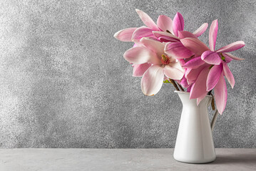 Still life with pink magnolia flowers in vase on gray concrete background with copy space. Wedding...