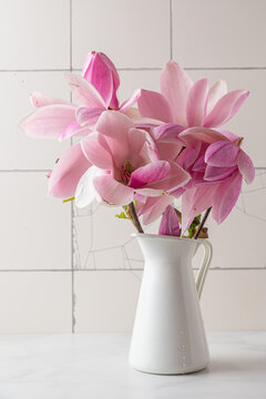 Still life with pink magnolia flowers in vase on white tile background. Vertical orientation. Wedding concept