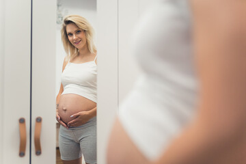 happy pregnant woman looking in the mirror at home, medium full shot pregnancy concept. High quality photo