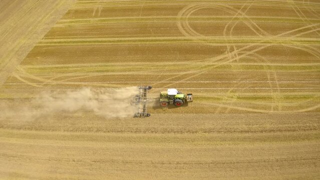 Tractor plowing field. Aerial view of moving tractor with plow raising dust.  Tractor plows ground on cultivated farm field. Farmer with tractor tilling the field to open the soil. 