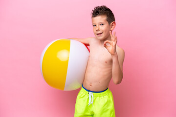 Little caucasian boy holding a beach ball isolated on pink background showing ok sign with fingers