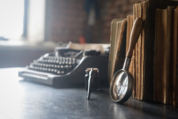 Retro style typewriter, stack of books, magnifying glass and inkpot with quill pen on the table....