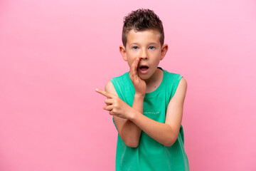 Little caucasian boy isolated on pink background pointing to the side to present a product and whispering something