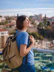 travel to Turkey, old town Antalya Kaleci. Happy asian female tourist traveller with backpack walks in old city. Woman on lookout over the old town and the port from viewpoint