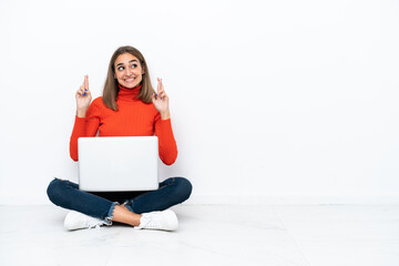 Young caucasian woman sitting on the floor with a laptop with fingers crossing
