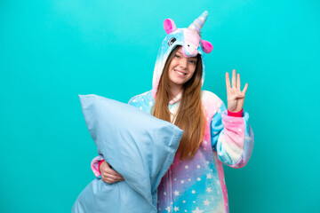 Young caucasian girl with unicorn pajamas holding pillow isolated on blue background happy and counting four with fingers