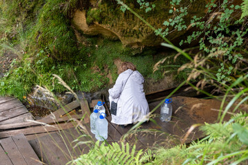 A woman fills five-liter containers with natural drinking water at a water source in the Gauja National Park, Latvia