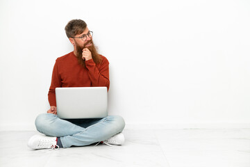 Young reddish caucasian man with laptop isolated on white background looking to the side and smiling