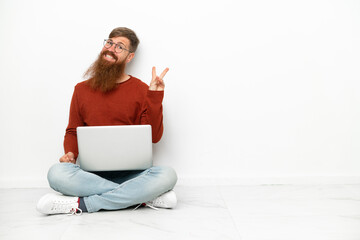 Young reddish caucasian man with laptop isolated on white background smiling and showing victory sign