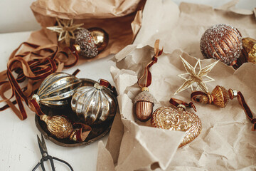 Merry Christmas! Stylish vintage christmas ornaments. Golden baubles, craft paper, ribbons and scissors on rustic white table. Moody banner. Preparation for winter holidays, atmospheric time