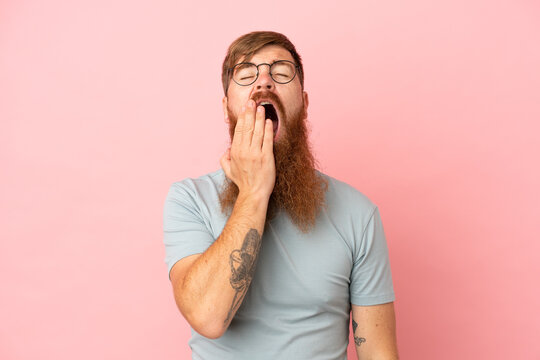 Young reddish caucasian man isolated on pink background yawning and covering wide open mouth with hand