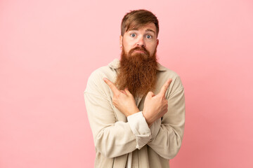 Young reddish caucasian man isolated on pink background pointing to the laterals having doubts