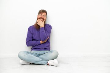 Young caucasian reddish man sitting on the floor isolated on white background smiling