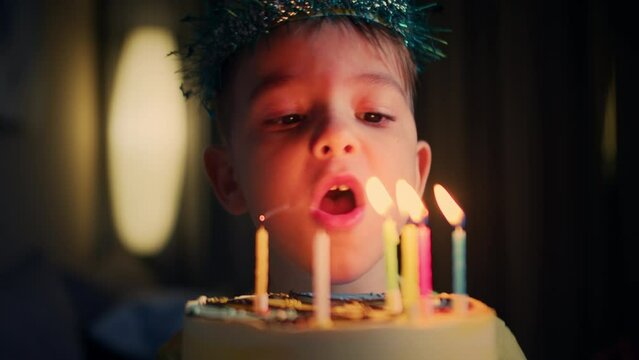 Close-up of charming caucasian little boy making wish and blowing candles on birthday cake. Portrait of happy pretty child celebrating birthday indoors at home. Joy and lifestyle