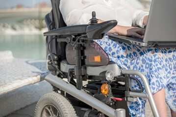 Close-up of a handicapped unrecognizable woman on wheelchair using laptop