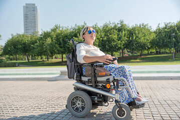 a smiling woman in an electric wheelchair takes a stroll on a sunny day through an urban park in the city