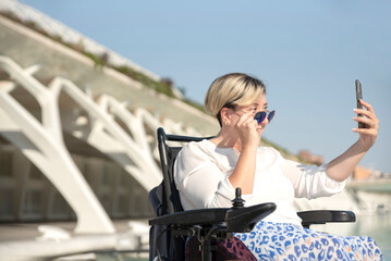 Fototapeta na wymiar portrait of a smiling disabled woman in a wheelchair taking a selfie looking behind sunglasses