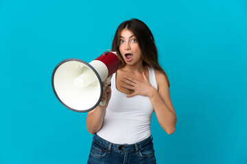 Young caucasian woman isolated on blue background shouting through a megaphone with surprised expression