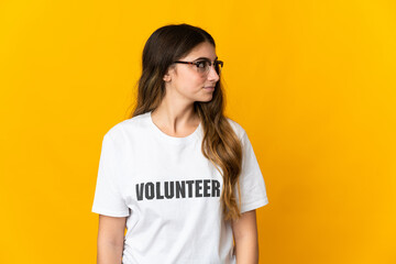 Young volunteer woman isolated on yellow background looking to the side