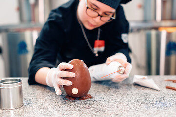 female chocolatier preparing a chocolate egg in her lab kitchen
