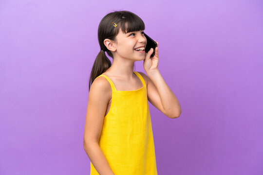 Little caucasian kid isolated on purple background keeping a conversation with the mobile phone