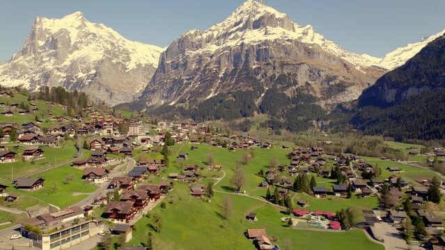 Aerial drone footage raising down and pushing out of Grindelwald village, with train and bus departing