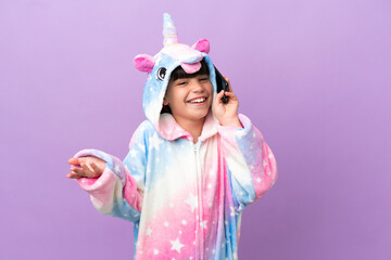 Little kid wearing a unicorn pajama isolated on purple background keeping a conversation with the mobile phone with someone
