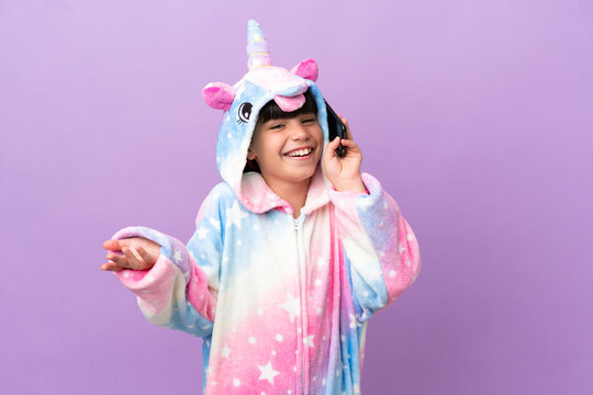 Little Kid Wearing A Unicorn Pajama Isolated On Purple Background Keeping A Conversation With The Mobile Phone With Someone