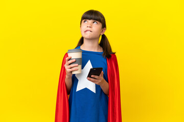 Little super hero kid isolated on purple background holding coffee to take away and a mobile while thinking something