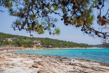 Amazing panoramic view of natural beauty turquoise clear sea water, pebbles beach, tourists on the beach on a summer day. Clear blue sky. Tripiti Beach, Greece island Thassos. 