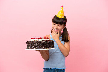 Little caucasian kid holding birthday cake isolated in pink background looking to the side and smiling