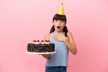 Little caucasian kid holding birthday cake isolated in pink background surprised and shocked while...