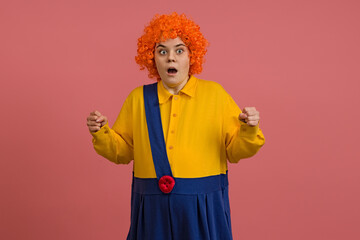 shocked girl in a clown costume and a bright wig on a colored background