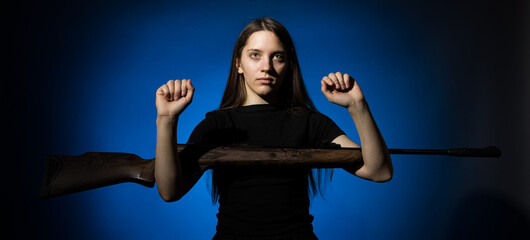 young beautiful woman with long hair in a black t-shirt holding a gun on a blue background